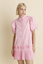 Woman wearing a pink dress with puff sleeves against a beige background