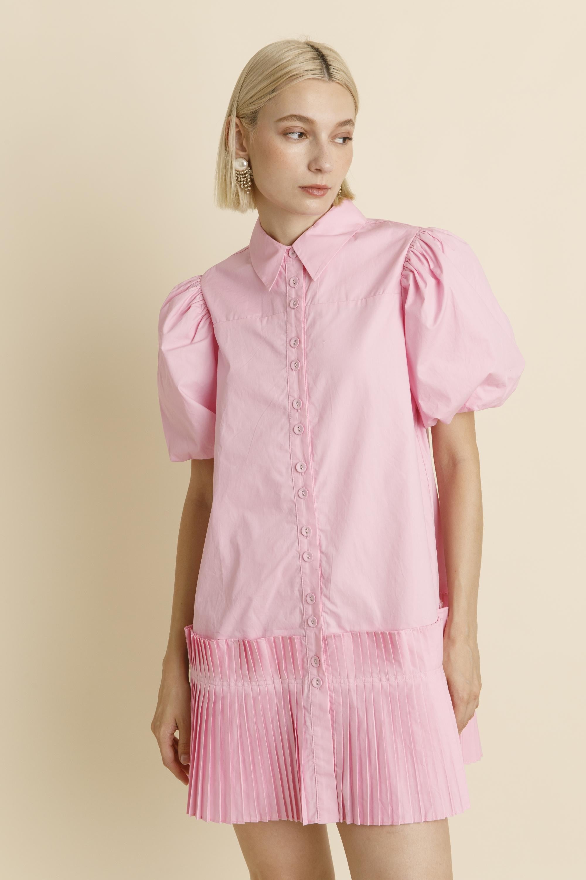 Woman wearing a pink dress with puff sleeves against a beige background