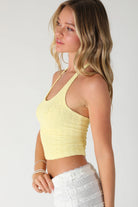 Woman wearing a yellow crop top and white pants against a plain background