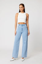 Woman wearing a white sleeveless top and light blue jeans on a white background