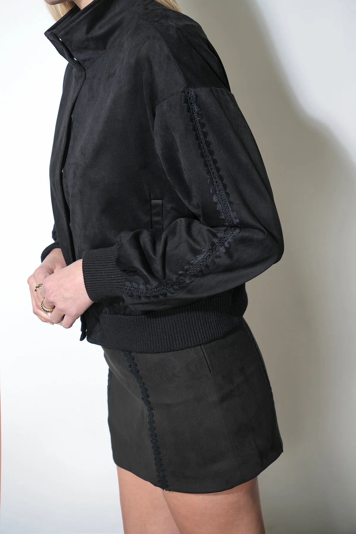 Person wearing a black jacket and skirt against a plain background