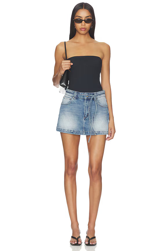 Woman wearing a black strapless top and denim skirt on a white background