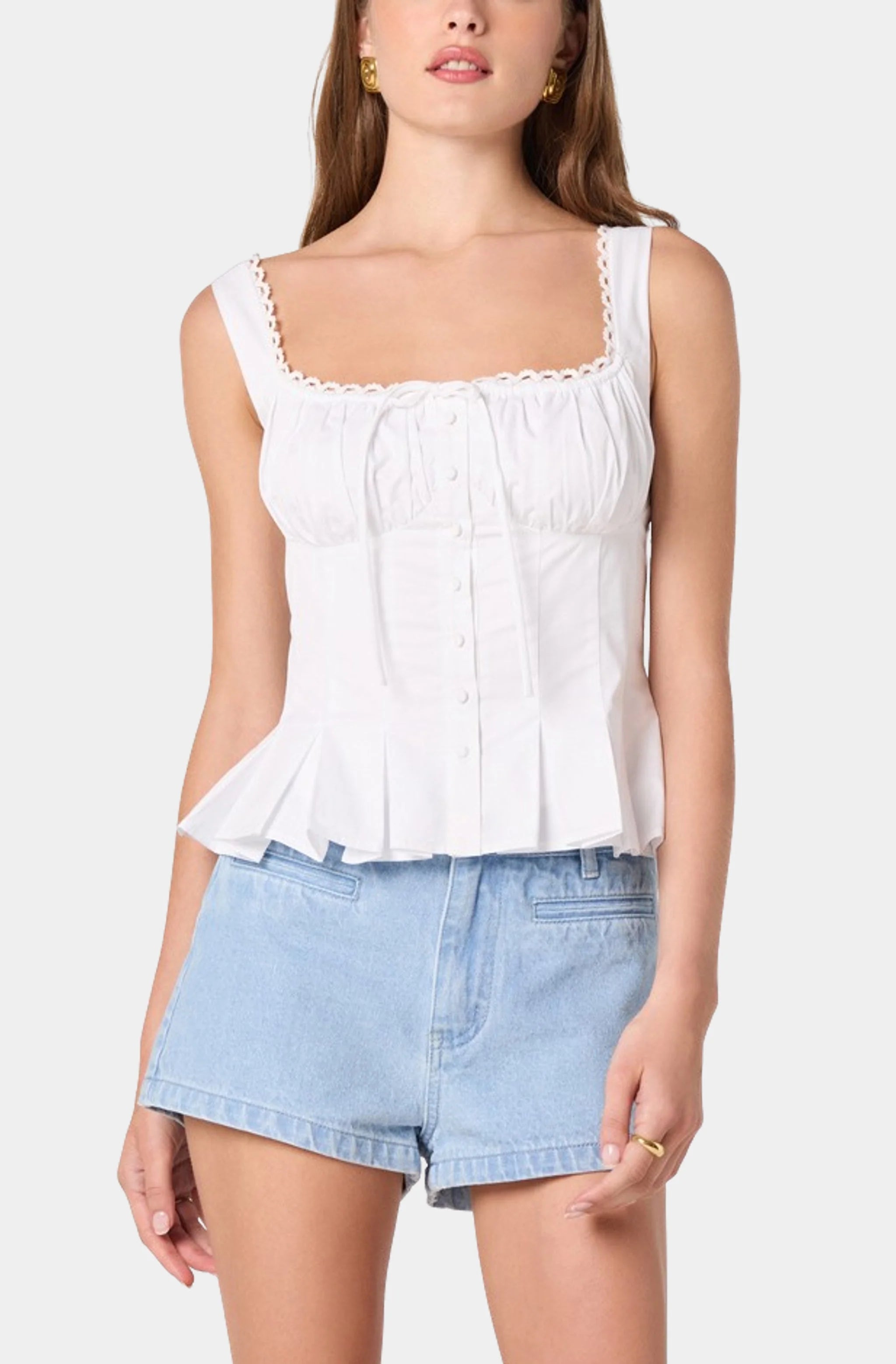 Woman wearing a white sleeveless top and light blue denim shorts on a plain background