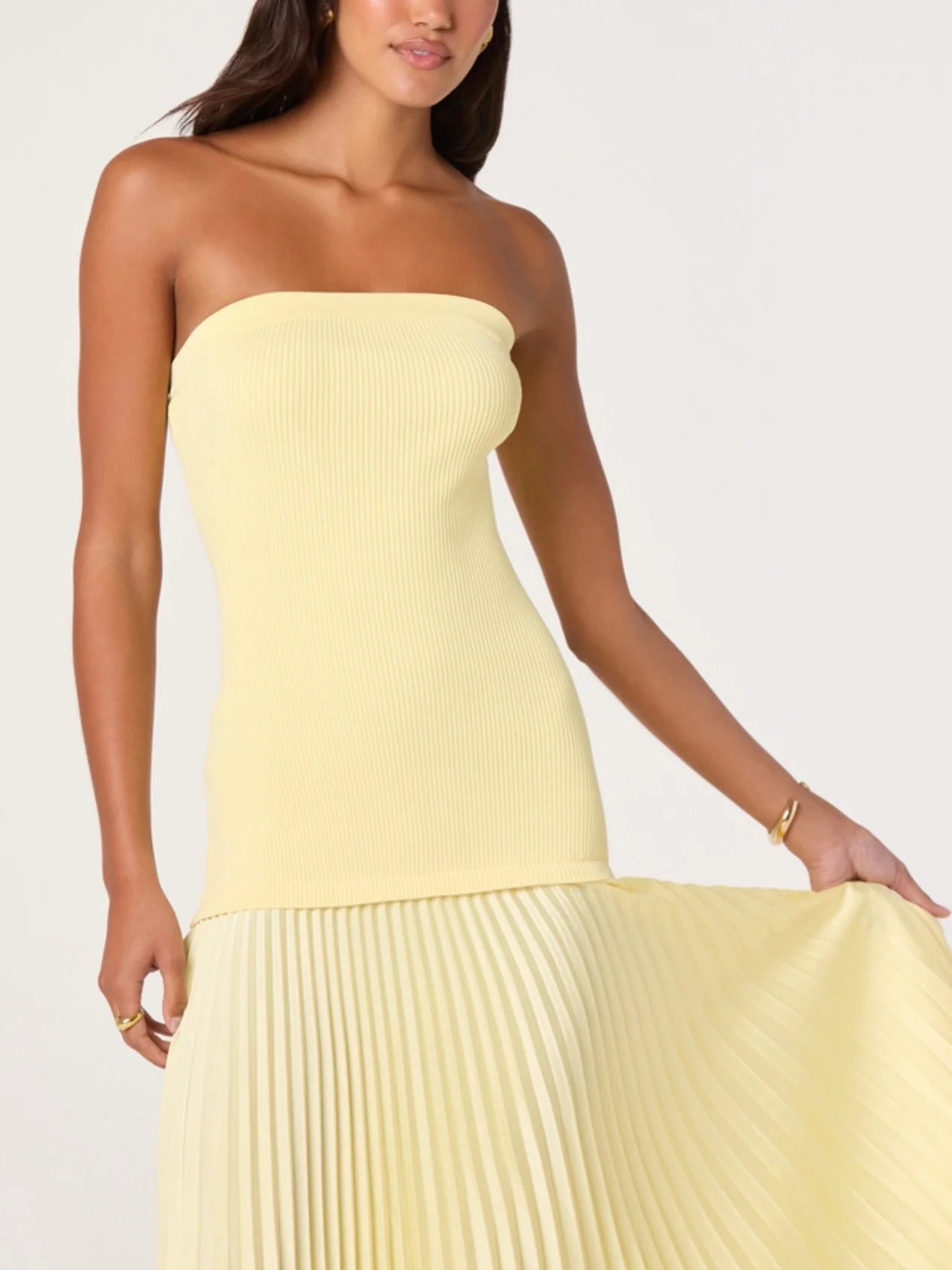 Woman wearing a strapless yellow dress with pleated skirt on a white background