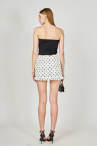 Woman wearing a black strapless top and white polka dot skirt on a plain background