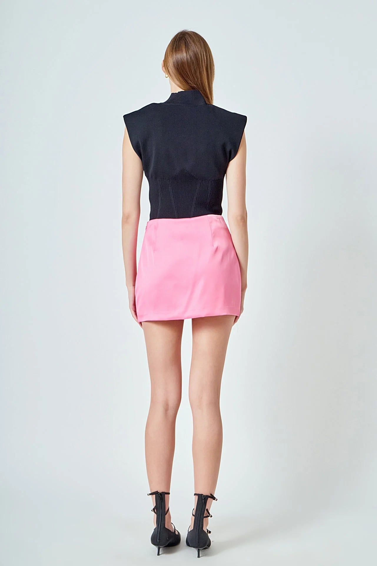 Person wearing a black sleeveless top and pink skirt on a white background