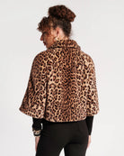 A woman shown from the back wearing a leopard-print faux fur cape jacket over a black top and black pants, against a plain white studio background.