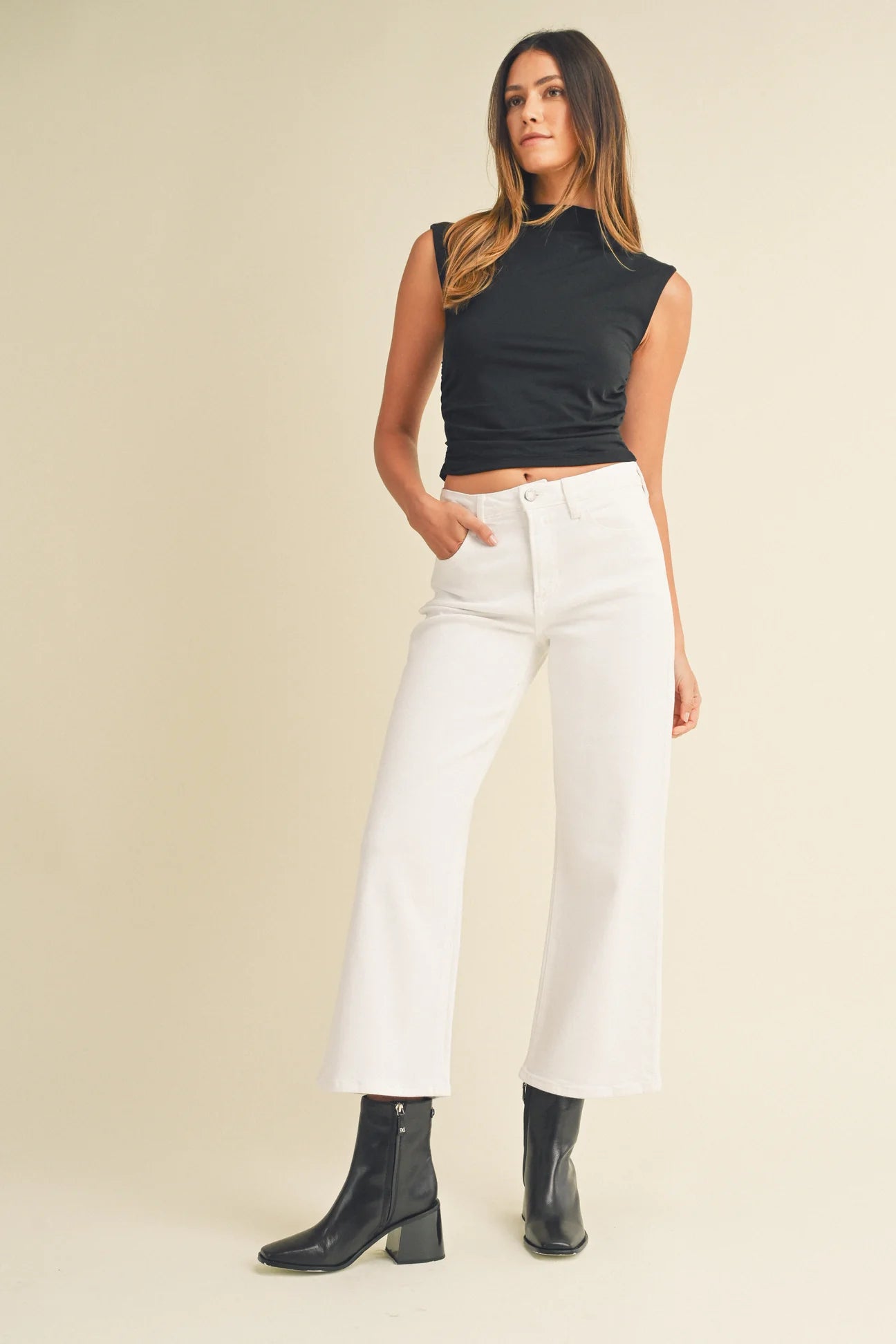 Woman wearing a black sleeveless top and white pants on a beige background