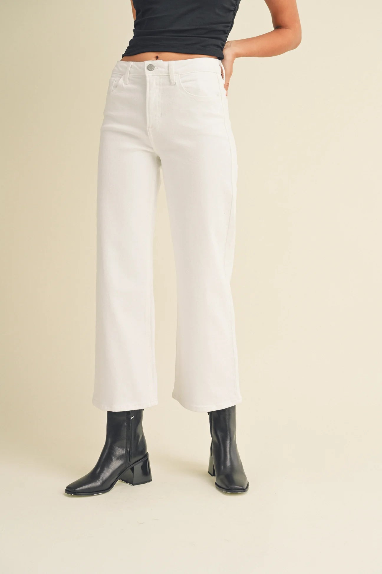 Person wearing white wide-leg jeans and black boots on a beige background