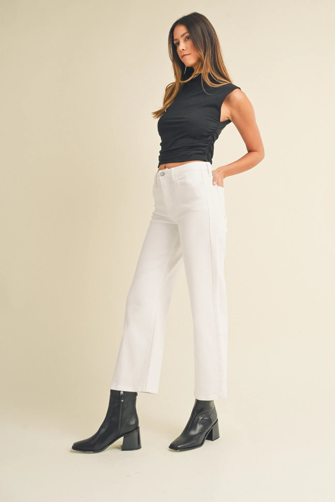 Woman wearing a black top and white pants with black boots on a beige background