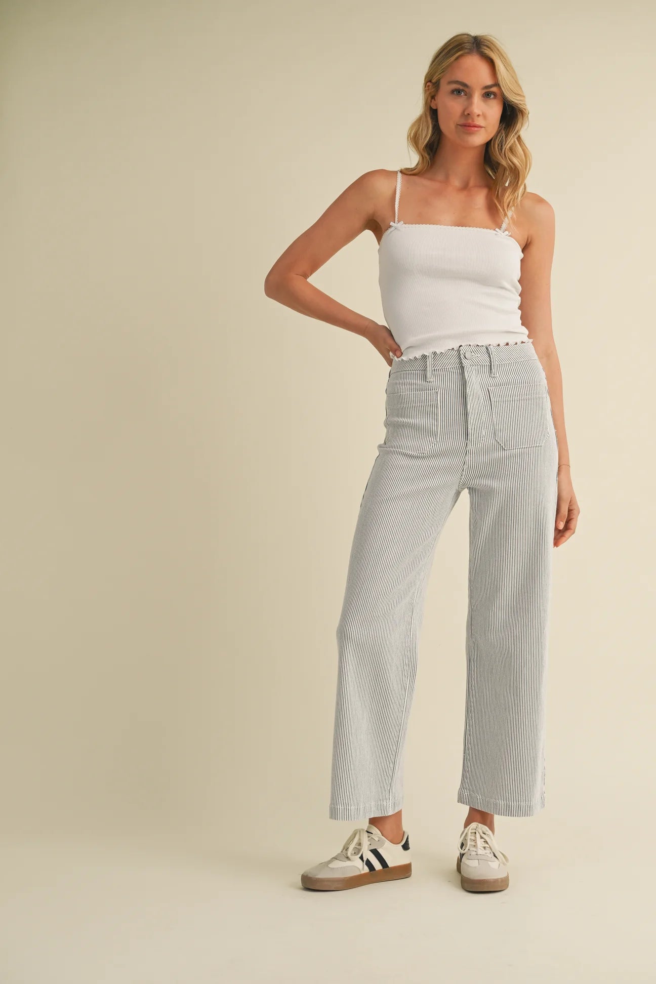Woman wearing a white tank top and stripe jeans against a beige background