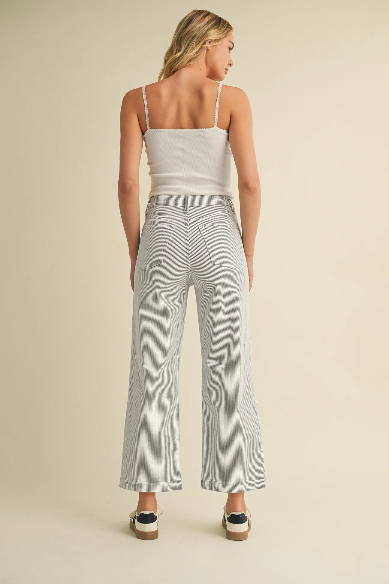 Woman wearing a white top and striped wide-leg pants on a beige background