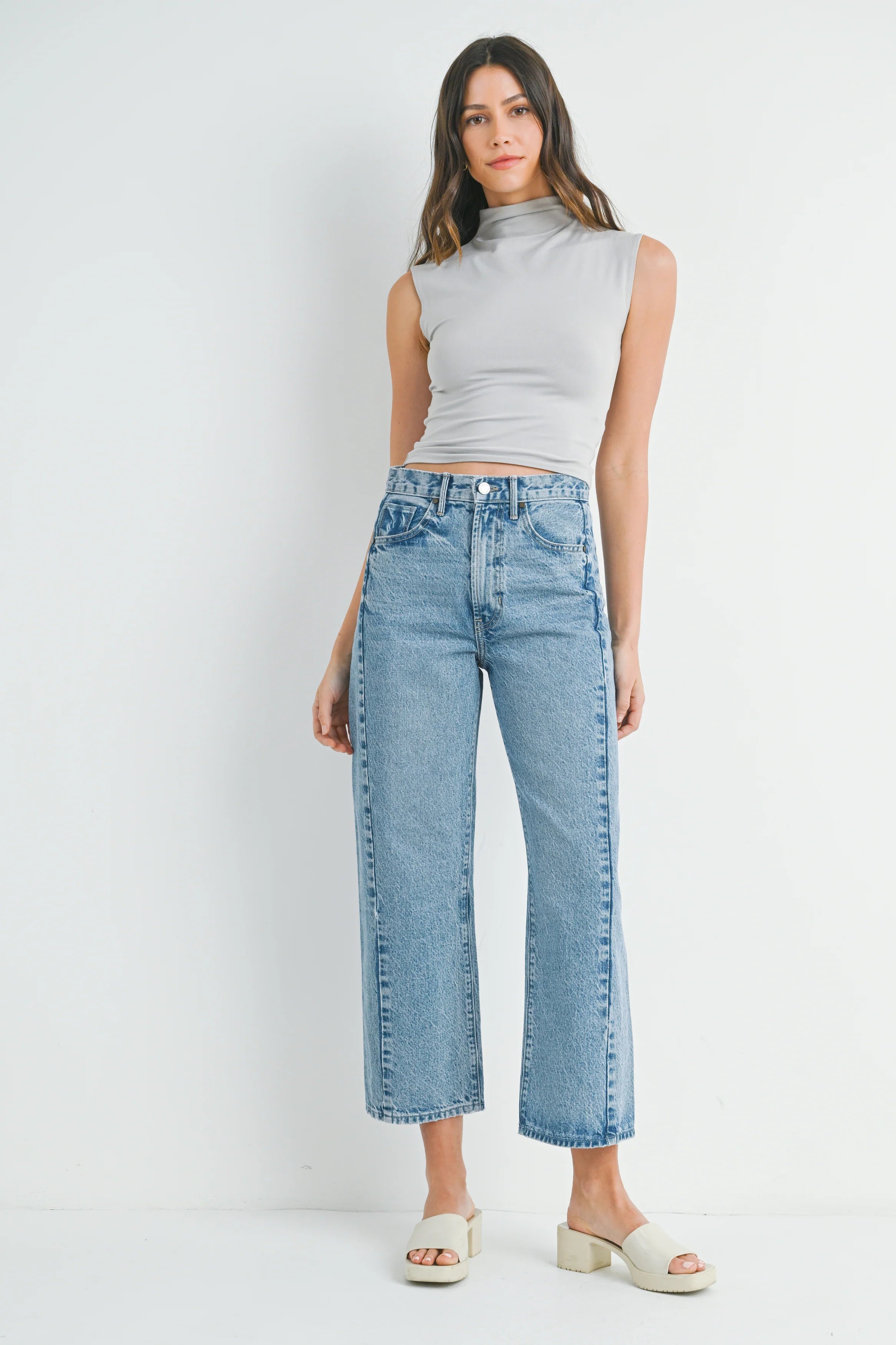 Woman wearing a sleeveless gray top and light blue jeans on a white background