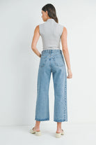 Woman wearing light blue jeans and a gray sleeveless top on a white background