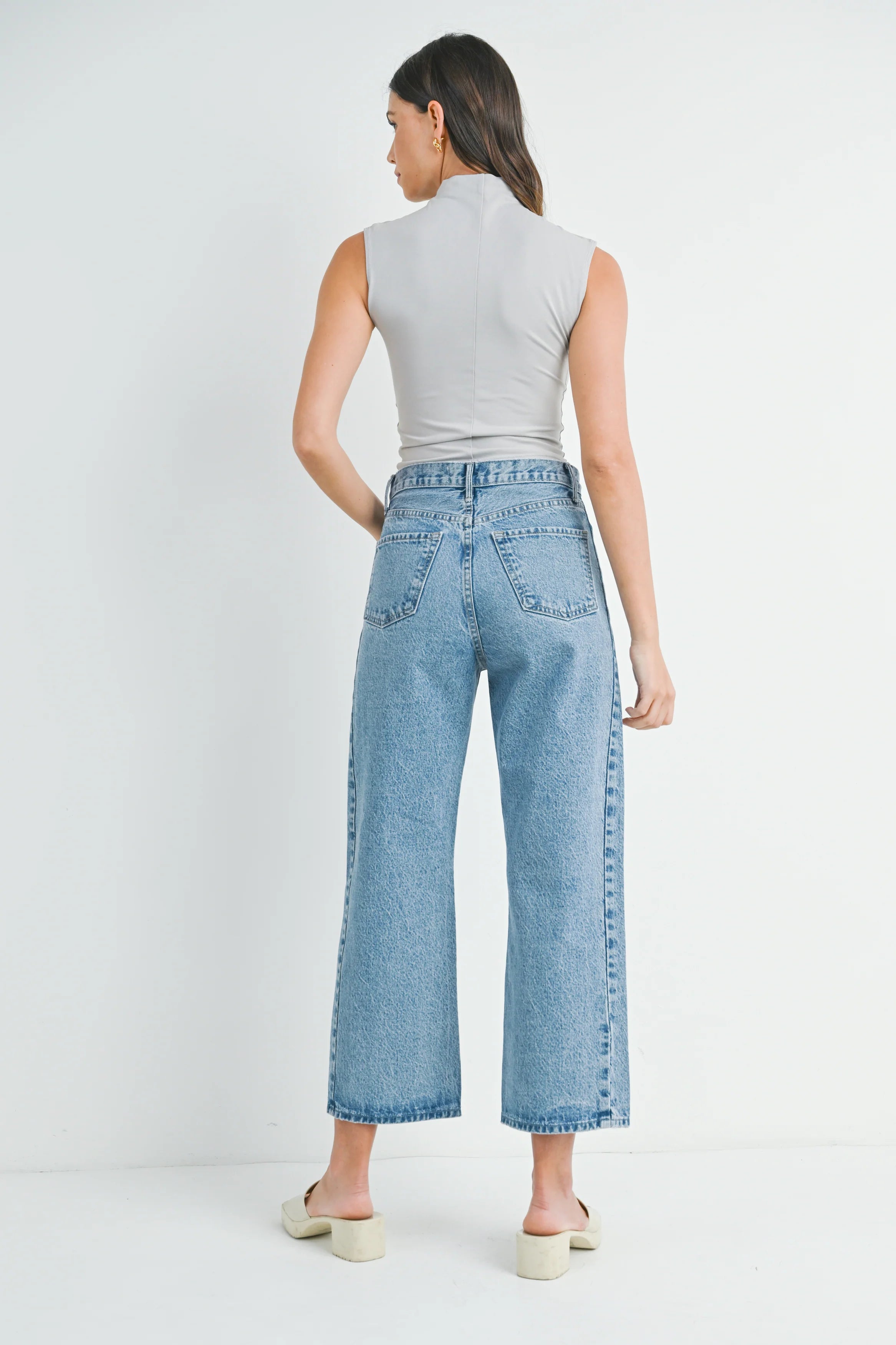 Woman wearing light blue jeans and a gray sleeveless top on a white background