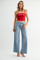 Woman wearing a red tank top and light blue jeans on a white background