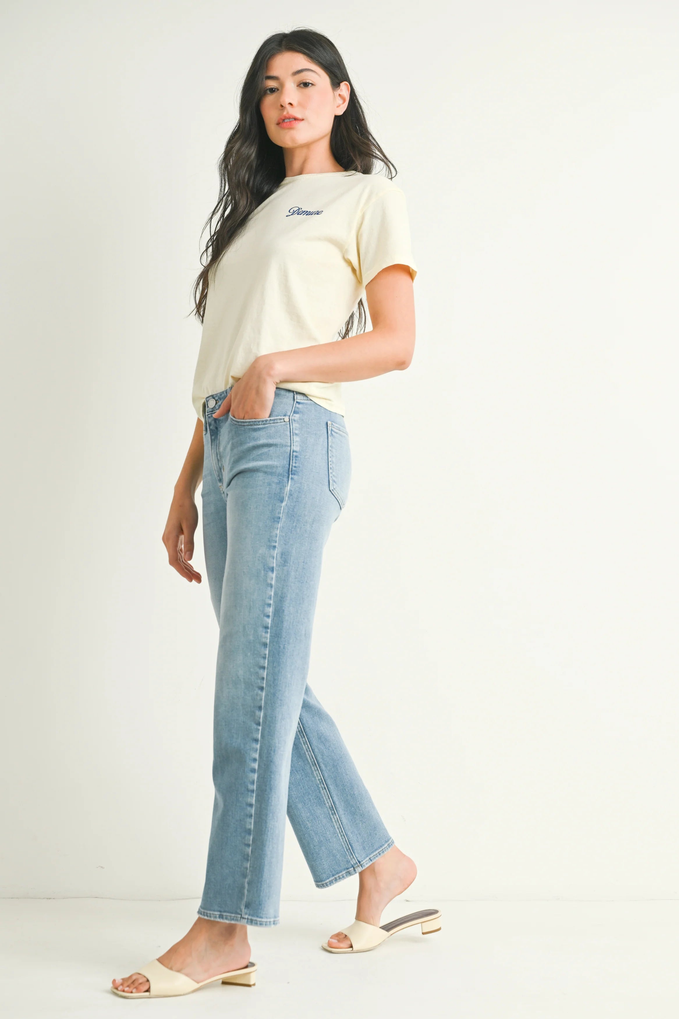 Woman wearing a cream t-shirt and light blue jeans on a white background