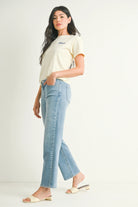Woman wearing a cream t-shirt and light blue jeans on a white background