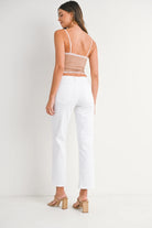 Woman wearing a beige open-back top and white pants on a plain background
