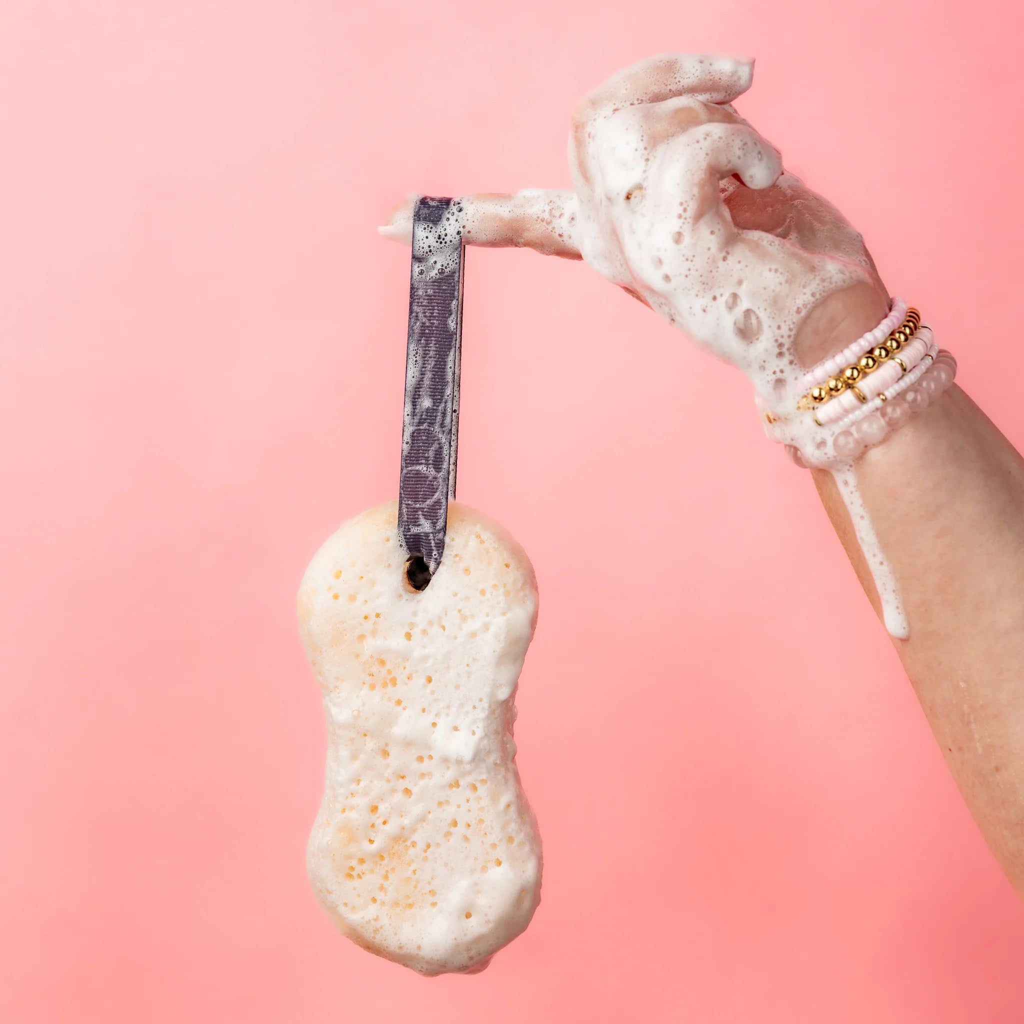 Hand holding a scrubber with soap suds against a pink background