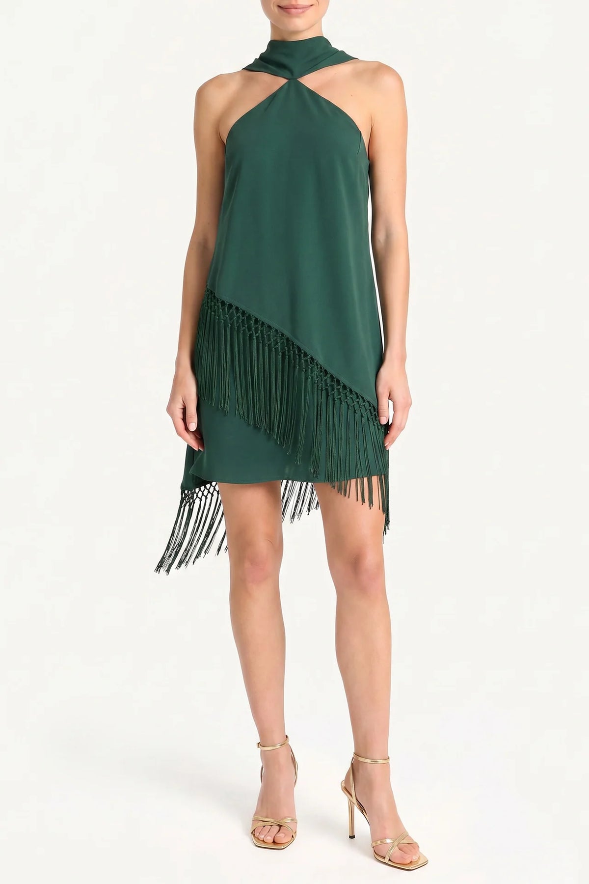 A woman models a dark green halter-neck dress with a diagonal fringe detail, paired with gold high-heeled sandals against a plain white studio background.