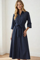 Woman wearing a navy blue dress with a belt against a white background