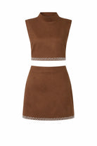 A two-piece brown suede-like set consisting of a sleeveless mock-neck crop top and a matching mini skirt, both featuring a decorative border of small white beads and metallic studs, shown against a plain white background.