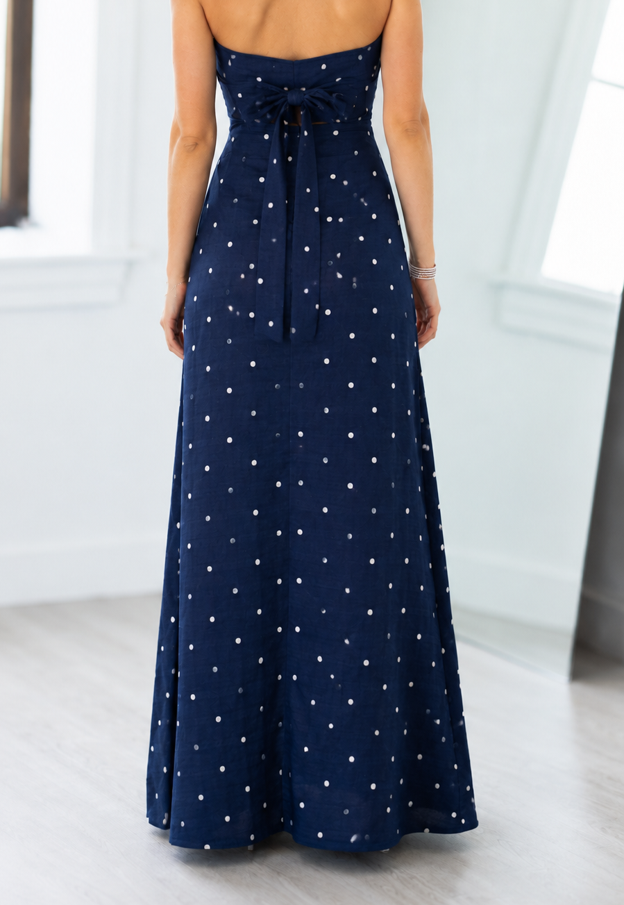 Woman wearing a strapless navy blue dress with white star patterns in a minimal indoor setting.