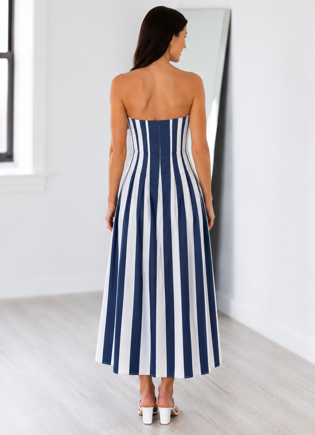 Woman wearing a strapless blue and white striped dress in a minimalistic setting.