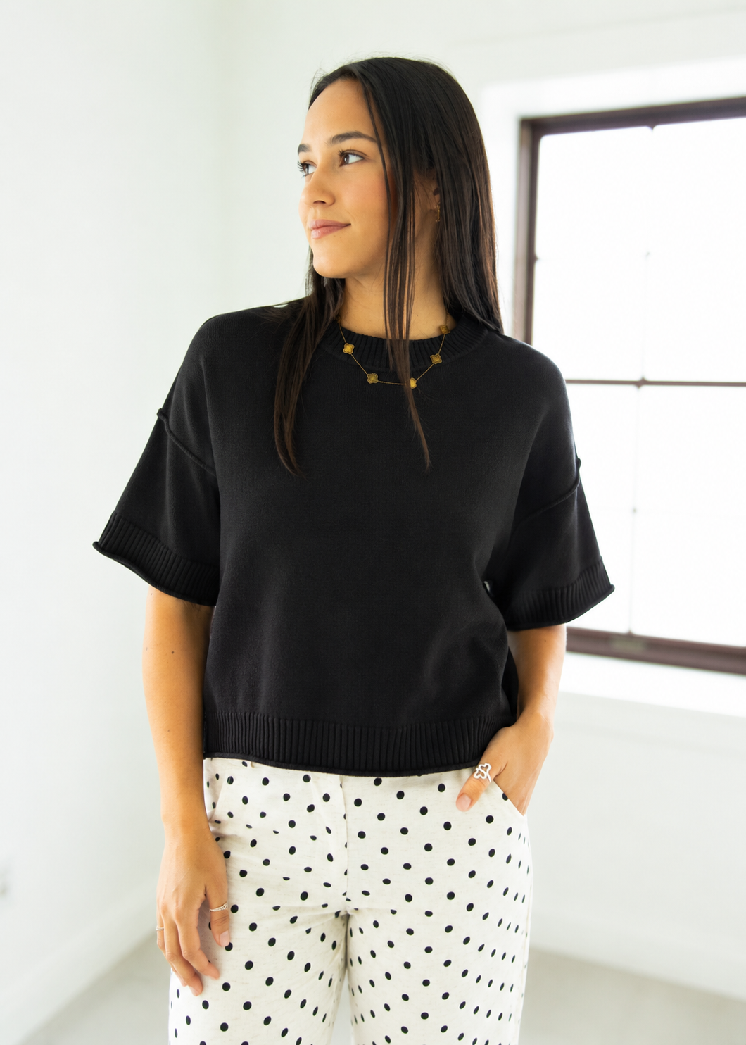 Woman wearing a black sweater and polka dot pants in a bright room.