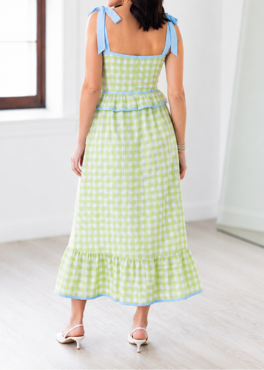 Woman wearing a green checkered dress with blue accents in a minimal indoor setting.