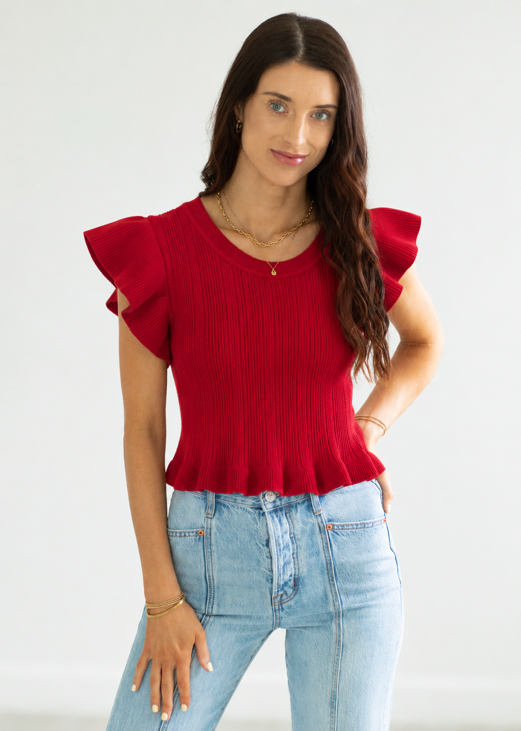 Woman wearing a red top with ruffled sleeves and light blue jeans on a white background