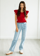 Woman wearing a red top with ruffled sleeves and light blue jeans on a white background