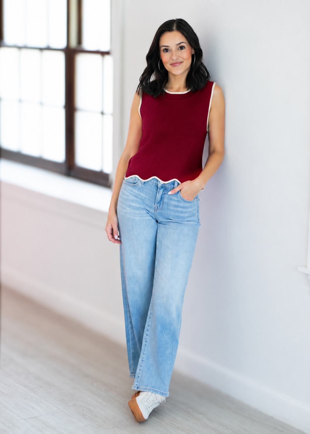 Woman wearing a red sleeveless top and light blue jeans standing indoors.