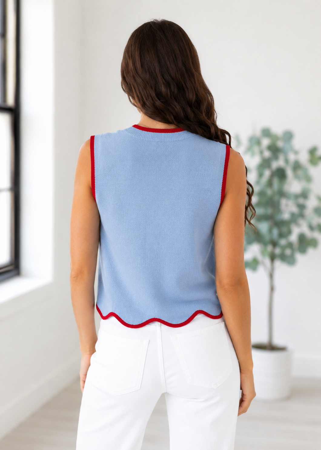 Woman wearing a light blue sleeveless top with red trim in a bright room.
