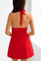 A woman shown from the back wearing a bright red halter-neck mini dress with a tie at the back of the neck and a fitted flared silhouette.