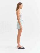 Woman wearing a white tank top and light blue denim skirt on a white background
