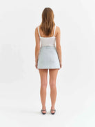 Woman wearing a white top and light blue denim skirt on a white background