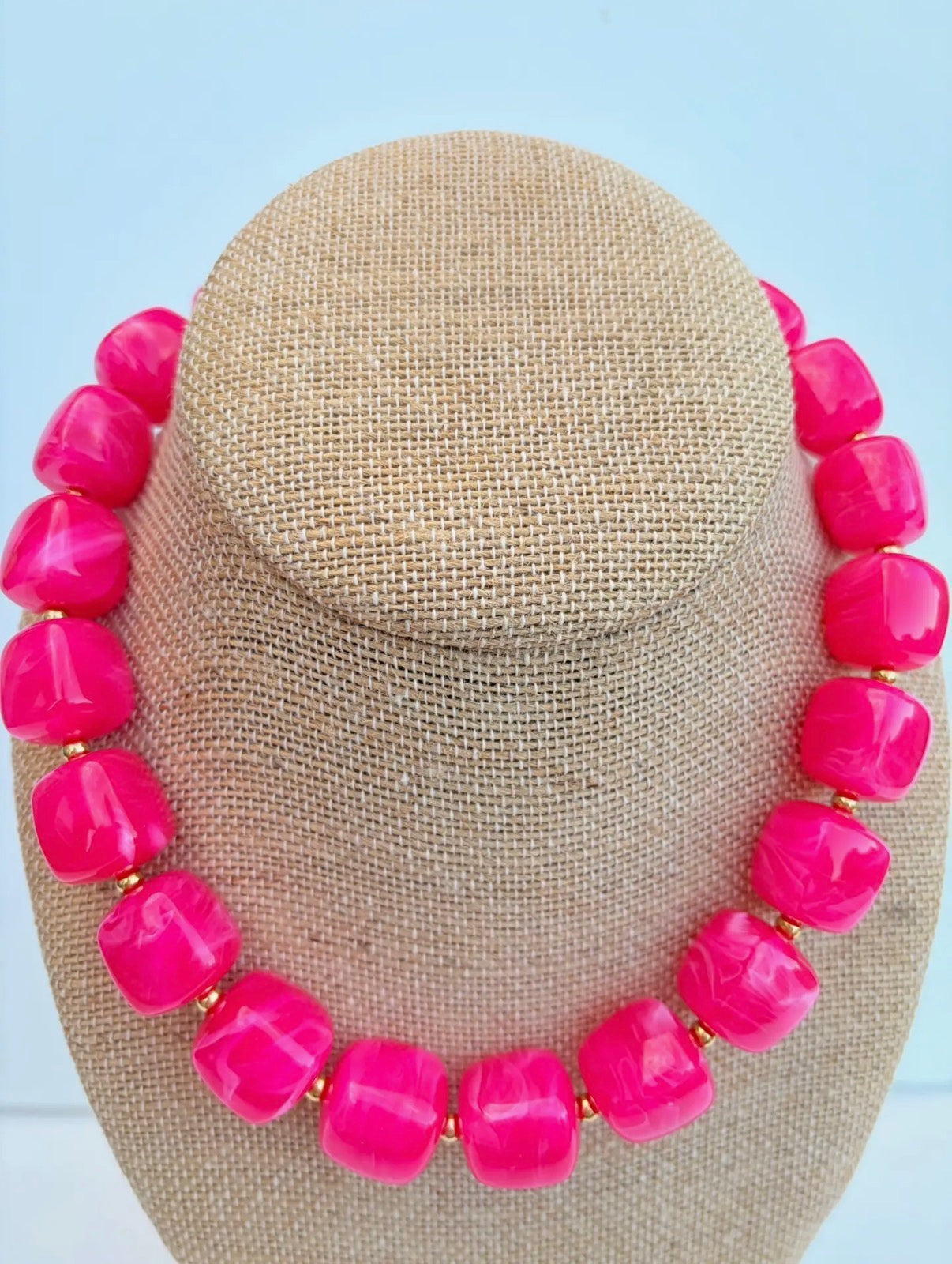 Necklace with bright pink beads on a beige display stand against a light blue background