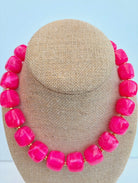 Necklace with bright pink beads on a beige display stand against a light blue background