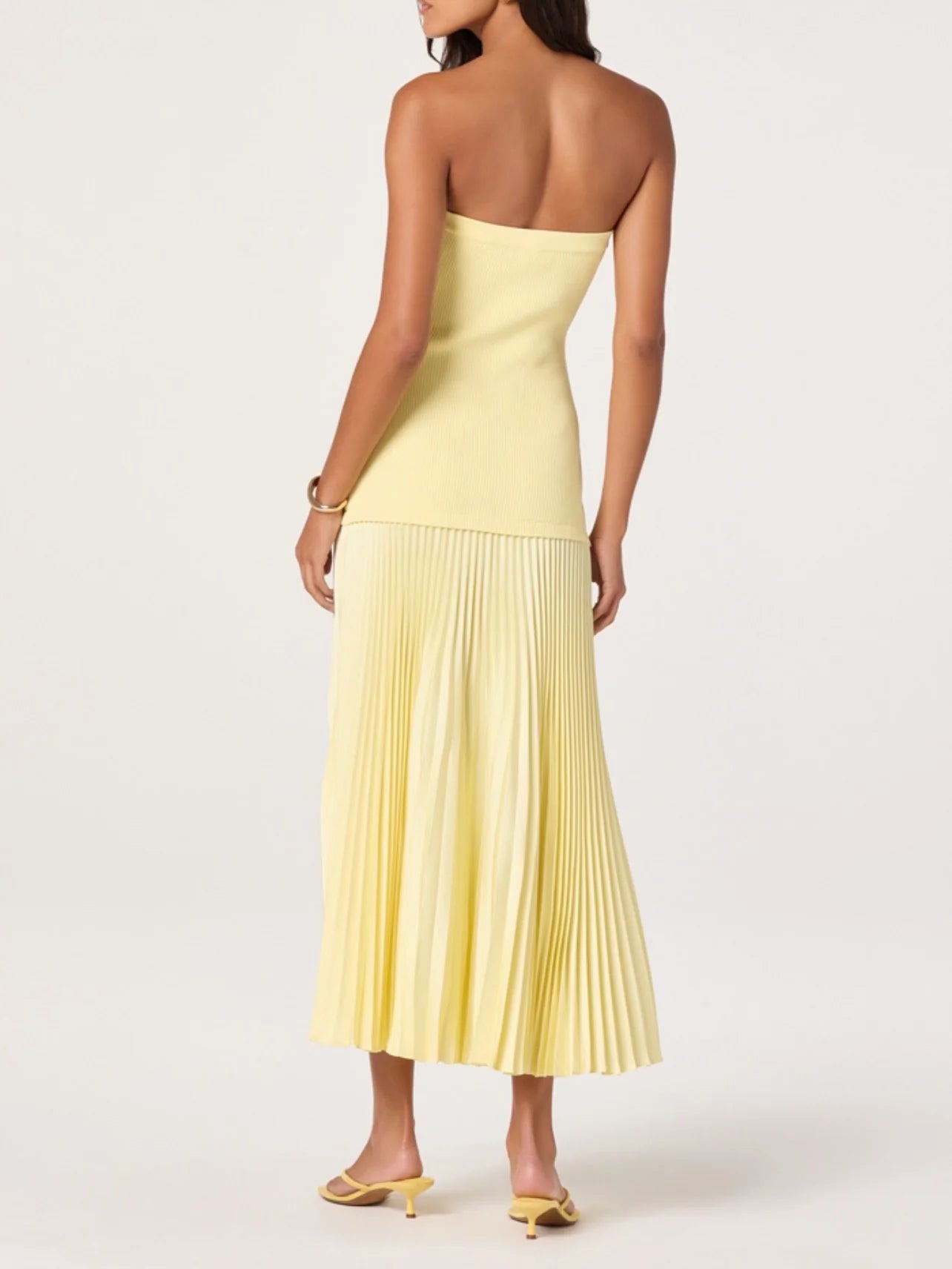 Woman wearing a strapless yellow dress with pleated skirt on a white background