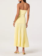 Woman wearing a strapless yellow dress with pleated skirt on a white background