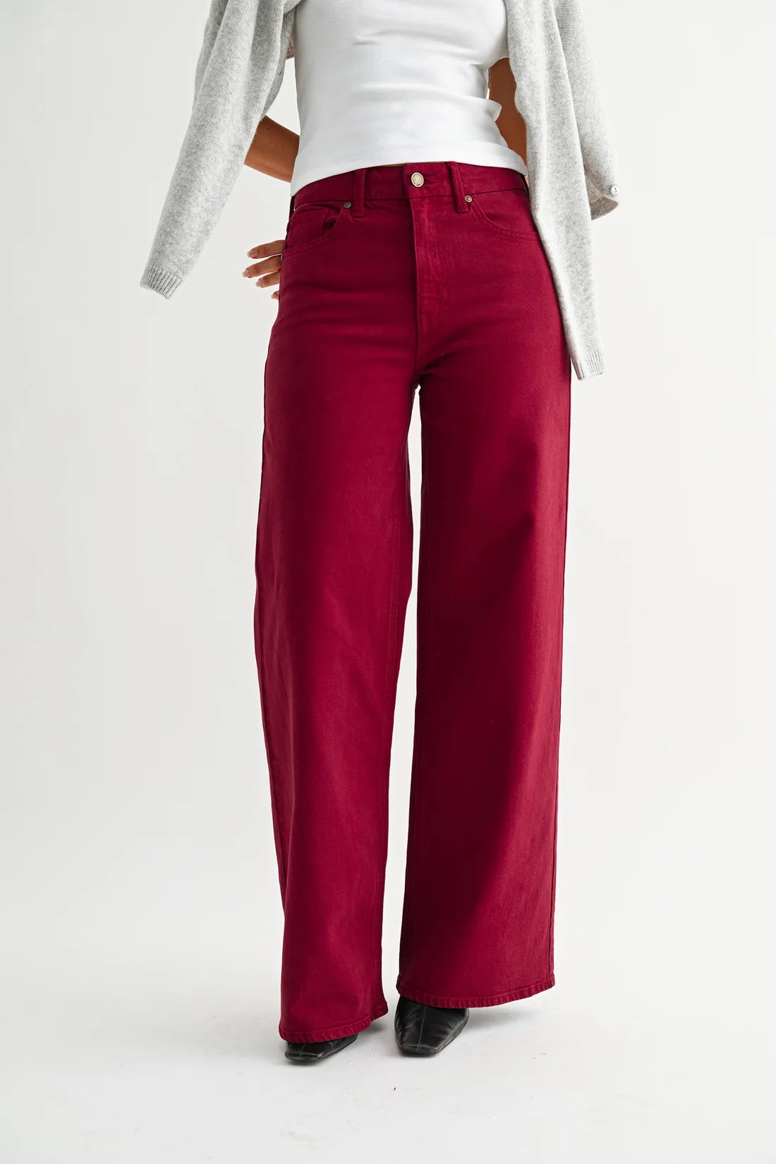A person wearing bright deep red wide-leg pants, styled with a white top and a light gray cardigan, shown from the chest down against a plain white studio background.