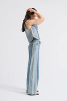 Woman wearing a light blue sleeveless top and wide-leg jeans on a white background