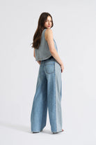 Woman wearing light blue jeans and a sleeveless top on a white background