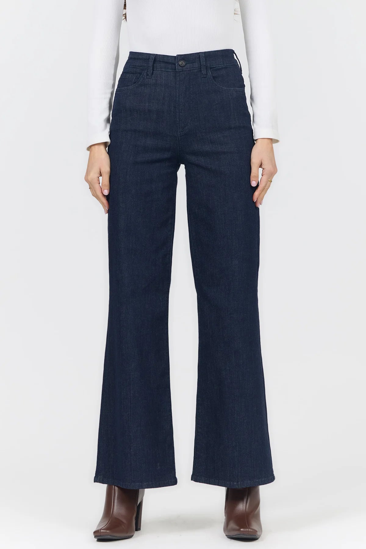 A model wearing dark blue wide-leg denim flare pants, paired with a white long-sleeve top and brown ankle boots, shown from the waist down against a light gray studio background.