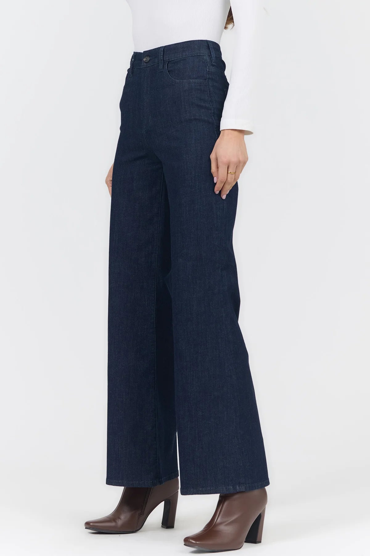 A person wearing dark blue wide-leg cropped pants with a white top and brown heeled boots, shown from the waist down against a plain light gray studio background.