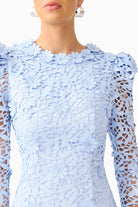 A close-up of a model wearing a light blue lace dress with long sheer sleeves and a high neckline.