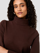 A close-up shot of a woman wearing a dark brown ribbed turtleneck sweater against a light gray background.