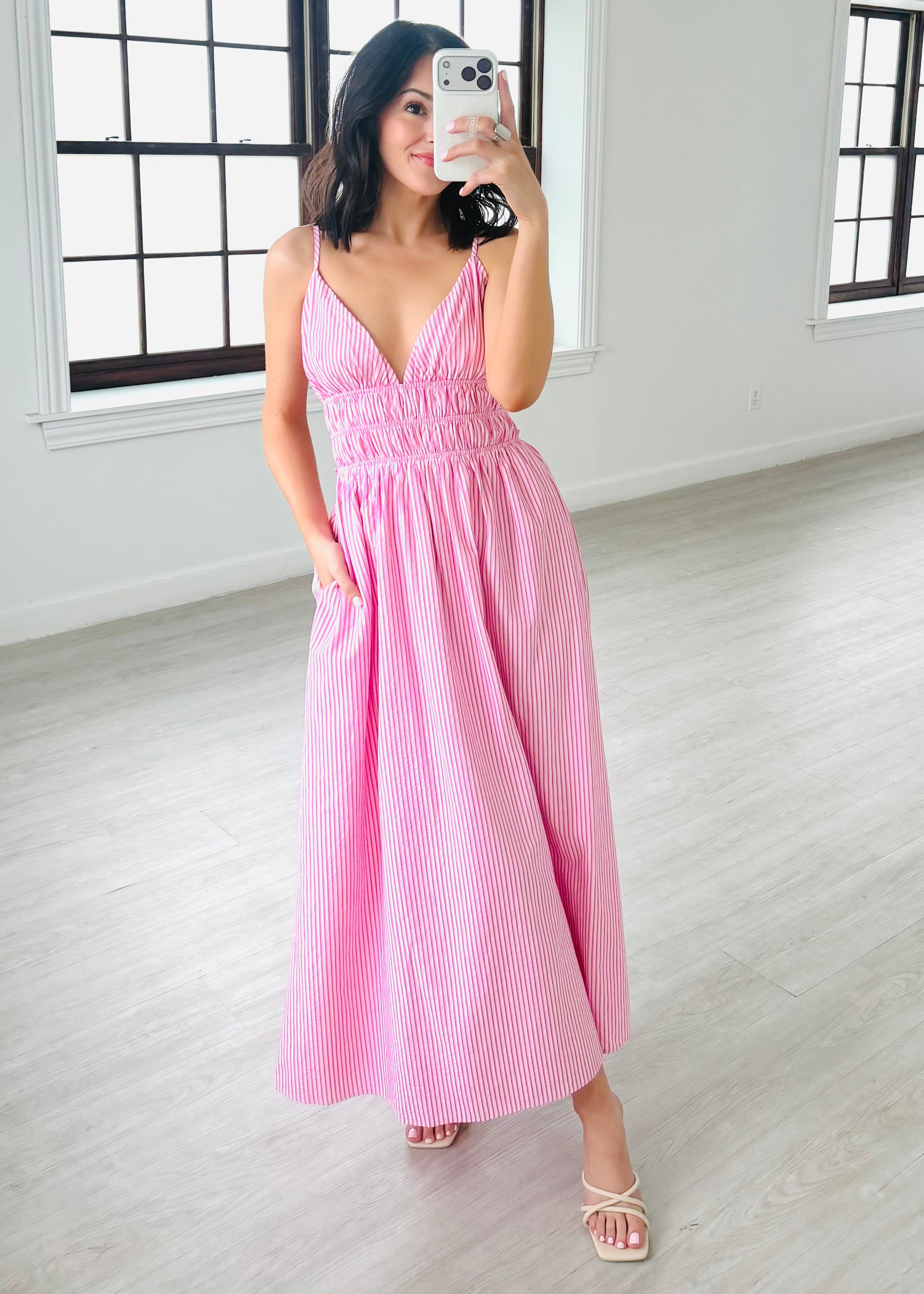 Woman in a pink dress taking a mirror selfie in a minimalistic room.